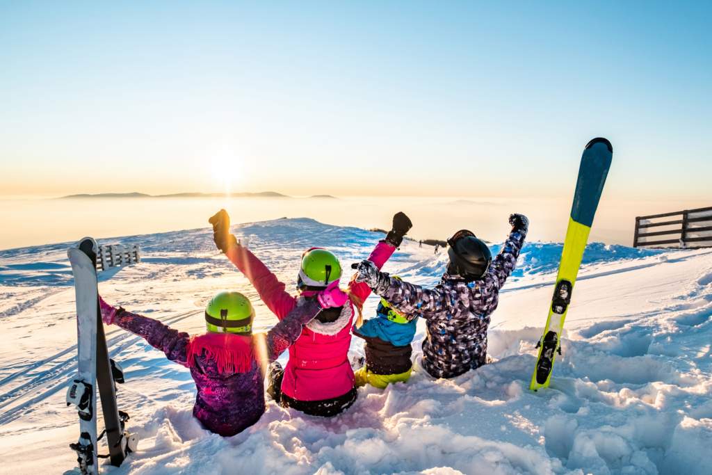 Apartmani Kopaonik Zoned - Porodica uživa u zimskim radostima, sedi na snegu sa snowboardima, sa slikovitim Kopaonikom u pozadini.