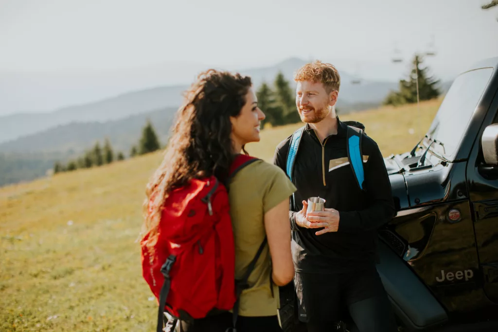 Hotel Kopaonik Zoned - Par u letnjem izletu na Kopaoniku, oslanjajući se na džip sa pogledom na zelene planinske padine.